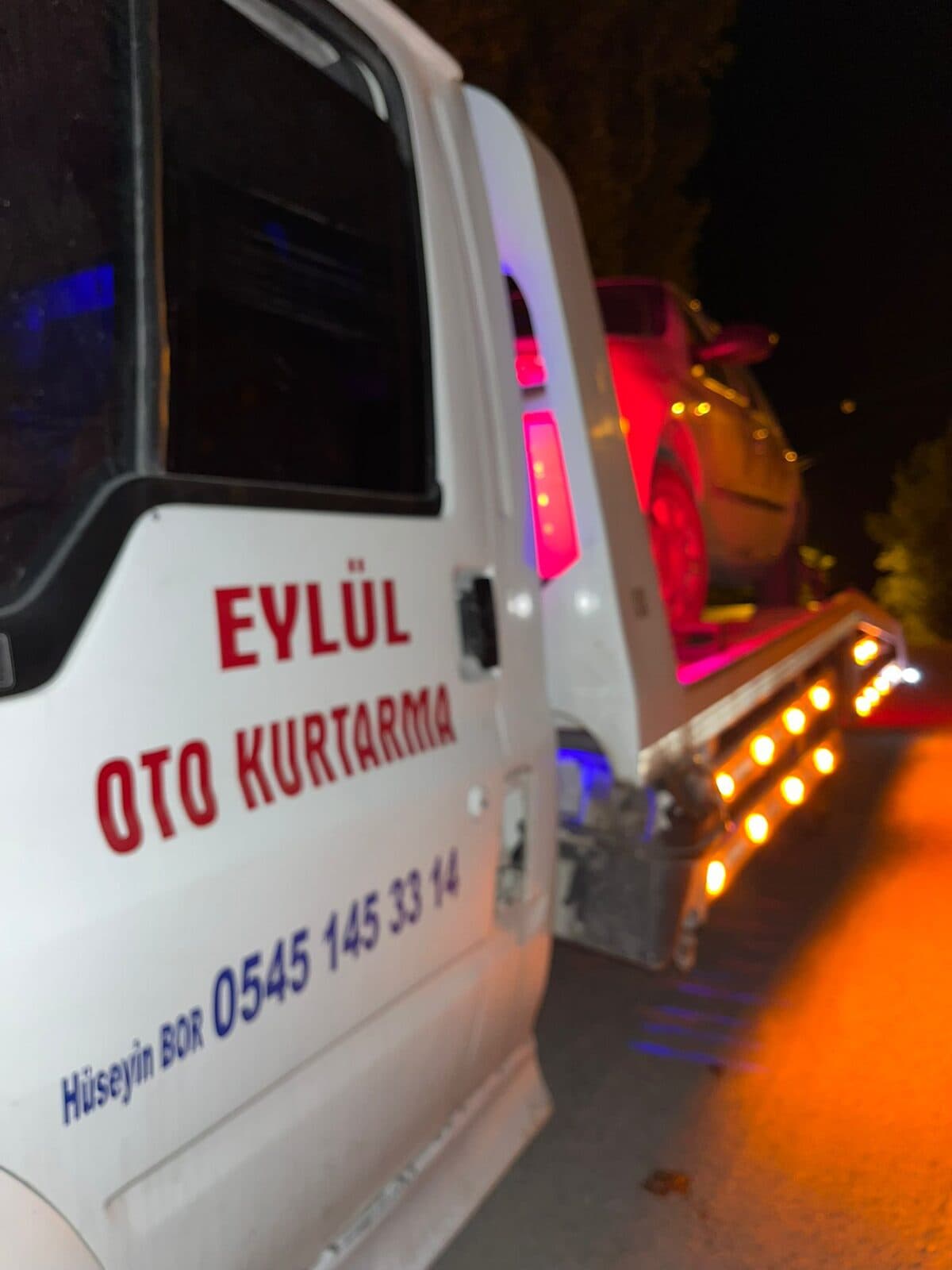 Eylül Oto Kurtarma yazılı çekici, gece ikaz lambaları yanarken araç taşırken